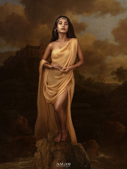"La Bella." A truly epic and artistic portrait. The subject, draped in golden fabric, stands against a painted backdrop of a stormy landscape, like a goddess from a myth.