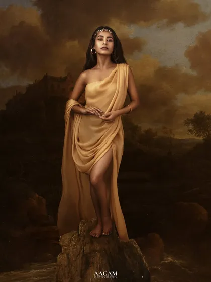 "La Bella." A truly epic and artistic portrait. The subject, draped in golden fabric, stands against a painted backdrop of a stormy landscape, like a goddess from a myth.