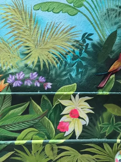 A close-up of the developing forest mural, showing the addition of colorful flowers and a small bird, bringing the scene to life.