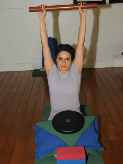 Here, a student uses a rod and weights to learn the correct action of the arms and shoulders. These props provide feedback, teaching the body to engage the right muscles and create stability and length, which is essential for healing.