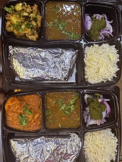Two different thali orders dispatched together. One has Jeera Aloo and the other has Chaap Masala, showing the variety available each day.
