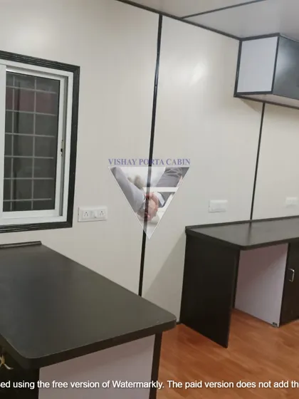 This image highlights a practical office interior with multiple desks and overhead storage. You can see the clean wall panels, durable flooring, and a sliding window with a security grill, making it a secure and functional workspace.