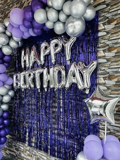 A simple yet striking birthday backdrop with a purple and silver balloon arch against a purple shimmer curtain.