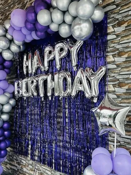 A simple yet striking birthday backdrop with a purple and silver balloon arch against a purple shimmer curtain.