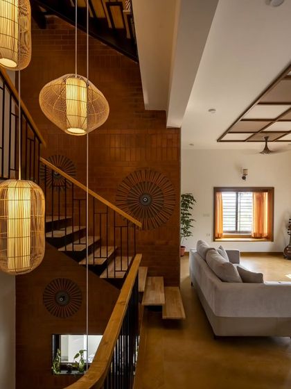 A view from the upper level into the Banashankari living room, showing how the staircase and double-height space are integrated. The cluster of cane lights adds a sculptural element.