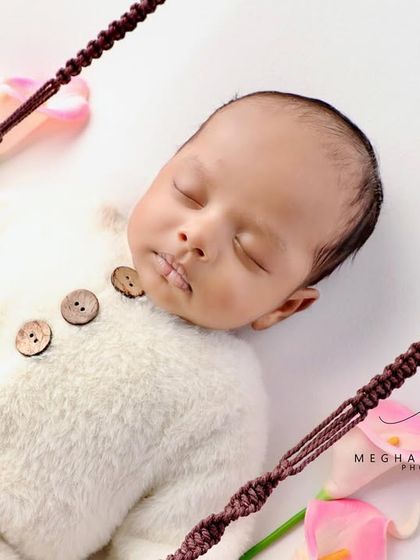A close-up of a baby in a fluffy white romper, sleeping on a miniature swing.