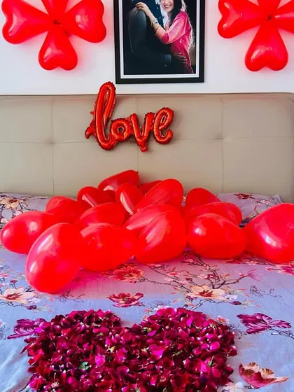 A close-up of the bed from the romantic room setup, showing a heart made of rose petals and a pile of heart-shaped balloons.