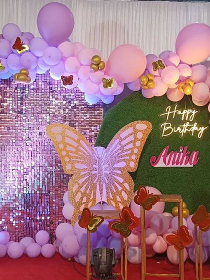 A beautiful butterfly theme with a purple shimmer wall and a grass backdrop. The decor includes a large butterfly prop, a Sofia the First cutout, and a purple balloon arch.