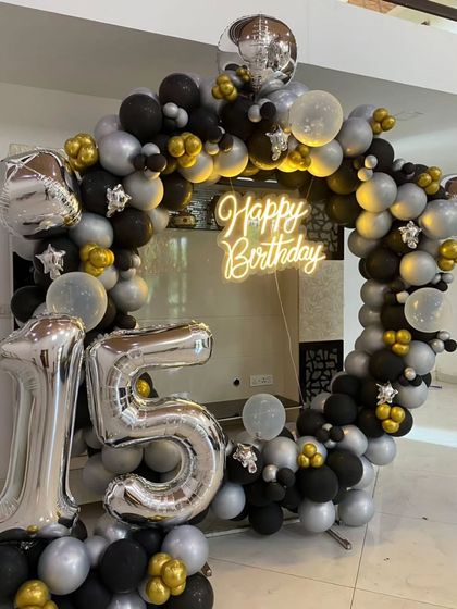 A 15th birthday setup with a black, silver, and gold balloon arch and large number balloons.
