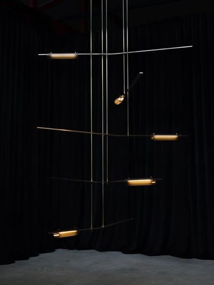 A large, multi-tiered Volant installation against a black curtain, its form resembling a complex mobile or kinetic sculpture.