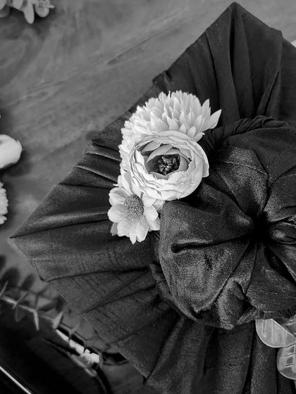 A black and white shot capturing the artistry of fabric wrapping. The soft folds of the material and the delicate floral embellishment highlight the quiet, handcrafted luxury that I pour into every piece.
