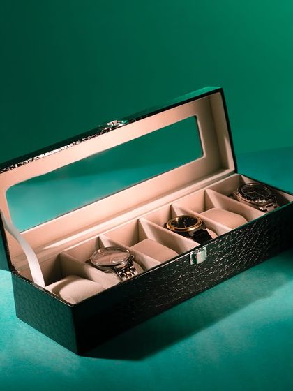 A watch box captured with dramatic, colored lighting against a deep green background, creating a moody and luxurious feel.