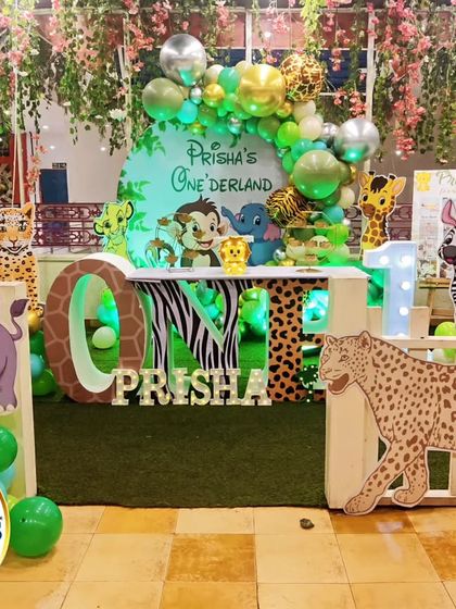 A full view of a "Prisha's Onederland" jungle party. The setup includes a 'ONE' table with animal-print letters, a picket fence, and numerous animal cutouts for an immersive experience.
