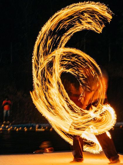 The long exposure captures the beautiful arc of fire created by a poi spinner. The raw energy of the flame is a powerful spectacle for everyone watching.
