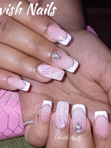 A modern French manicure with a twist, featuring silver glitter tips, marble art, and rhinestone accents.