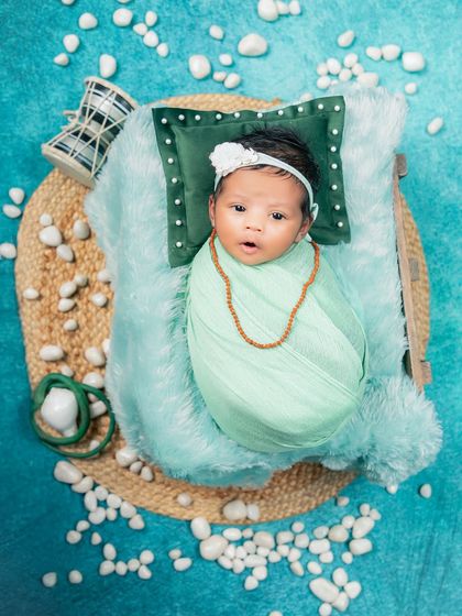 An overhead shot of the Maha Shivratri theme, providing a full view of the creative setup. The baby is swaddled and lies on a jute mat surrounded by white pebbles, a damru, and a soft pillow.