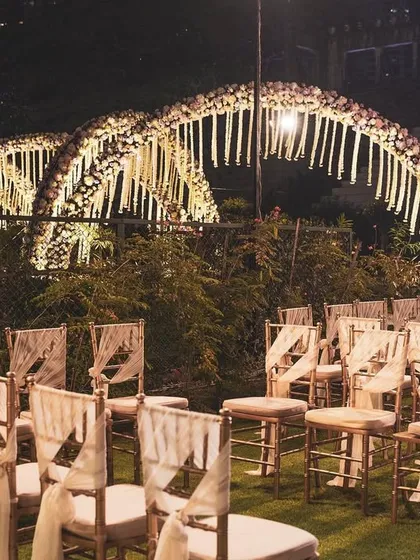 An intimate wedding seating arrangement around a floral arch mandap. The design uses hanging floral strings and elegant chairs to create a beautiful and personal ceremony space.