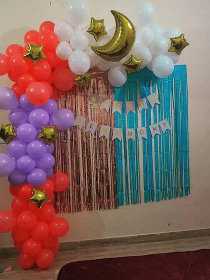 A simple and sweet backdrop for a baby's naming ceremony. The decoration includes a colorful balloon arrangement with a moon and stars theme against a tinsel curtain.