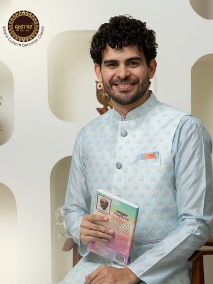 Where custom becomes classic. A model in a light blue printed Nehru jacket, holding a book, presents a look of intellectual charm and style.