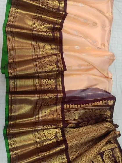 A beautiful pure Gadwal silk handloom saree in a pastel peach color with a rich, dark traditional border.