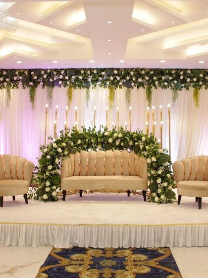 A classic stage setup with a floral arch and elegant seating at Grand Utsav banquet. The candle-like lights add a warm and romantic glow to the backdrop.