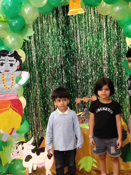 Children standing before our festive Janmashtami backdrop, complete with Krishna and cow cutouts and a green balloon arch.