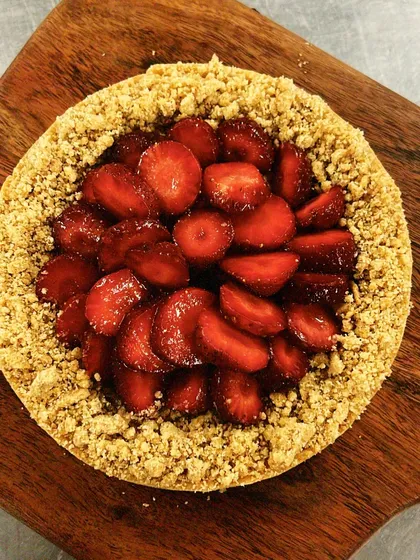 A rustic strawberry tart with a delicious crumble border, resting on a wooden board. The beauty of this dessert is in its simplicity and fresh flavor.