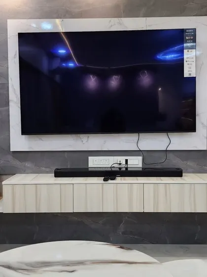 A detailed shot of the TV unit, highlighting the combination of light wood laminate, a marble-finish frame, and vertical fluted panels.