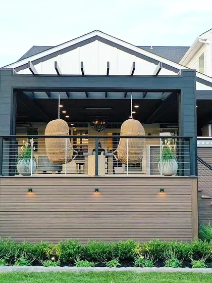 This inspirational two-story deck design showcases a modern farmhouse aesthetic. It features a covered upper lounge with hanging chairs and an open lower deck, demonstrating how we can create multi-level outdoor living spaces.