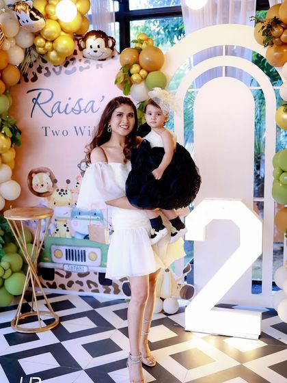 A mother and daughter pose in front of the "Raisa's Two Wild" birthday backdrop. This photo shows the scale of the setup and how it serves as a perfect background for family pictures.