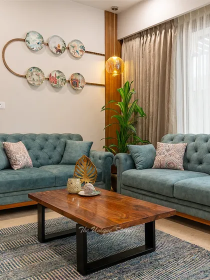 We designed this living area to reflect a modern Indian contemporary aesthetic, perfect for a young couple. The space features elegant teal tufted sofas, a solid wood coffee table, and unique ceramic plate wall decor, creating a warm and stylish environment that feels both timeless and fresh.