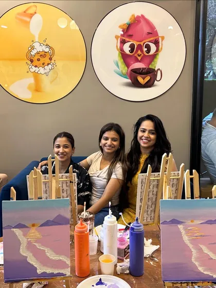 Three friends posing behind their easels, their beach-themed paintings just getting started.