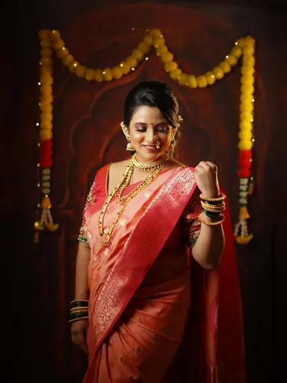 A candid portrait of a woman in a beautiful pink saree, smiling gently under a traditional marigold flower decoration during a Diwali shoot.
