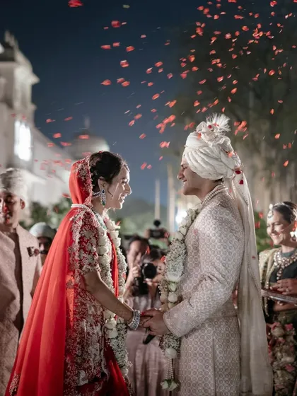 Anaaya and Nikunj share a moment during their varmala ceremony, surrounded by falling petals and the happy faces of their loved ones. The evening light adds a magical glow to their connection.