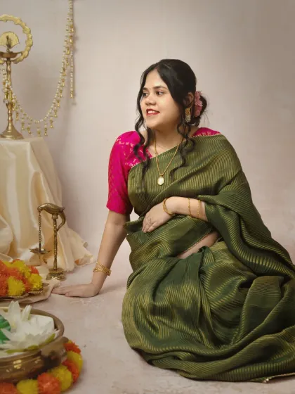 A candid solo shot of the mother-to-be, looking off-camera with a gentle smile. The soft lighting and the rich color of her saree make this a beautiful, reflective portrait.