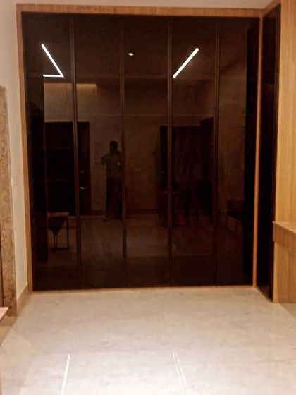 This wardrobe features dark, highly reflective glass shutters that blend seamlessly with the adjacent wood paneling. The integrated dressing table makes it a complete, functional space.