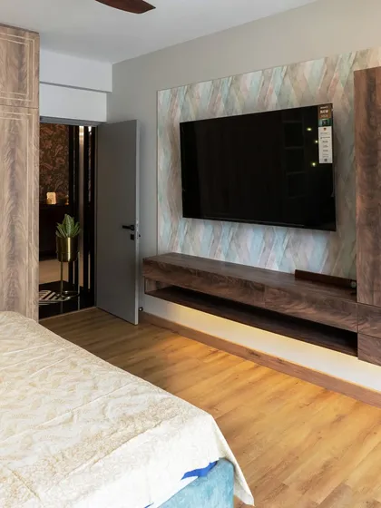A view of the bedroom's media wall, featuring a floating TV console and integrated wardrobe. The mix of dark wood and a lighter, patterned wallpaper behind the TV adds visual interest and texture.