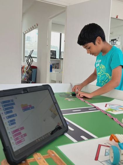 A student programs his robot using a tablet, with the code visible on the screen. This image highlights the integration of digital skills with physical building in our IRO training.