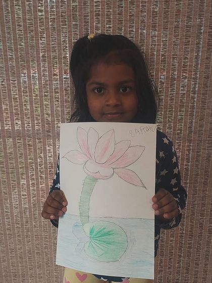 A young artist proudly holds her delicate drawing of a lotus flower.
