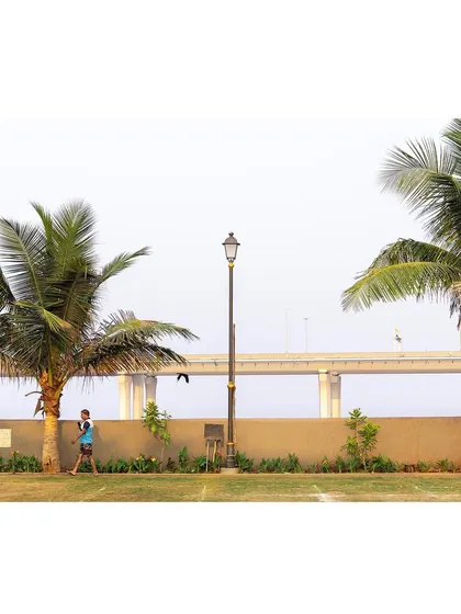 A lone walker enjoys the pathway at the Worli ground, with the iconic Bandra-Worli Sea Link in the distance. The design connects the local community space to the larger context of the city of Mumbai.