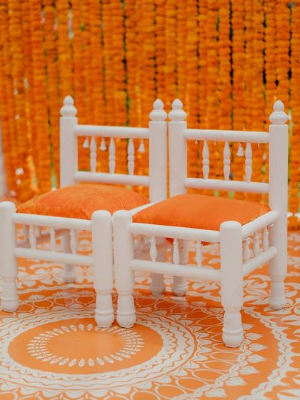 A close-up of the traditional white 'patla' seating for the bride and groom, set against the marigold backdrop.