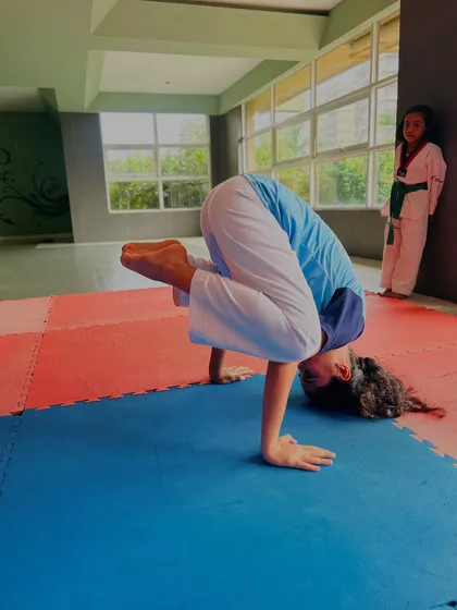 A student performs a crow pose, a yoga asana that builds arm and core strength, which is vital for Taekwondo.