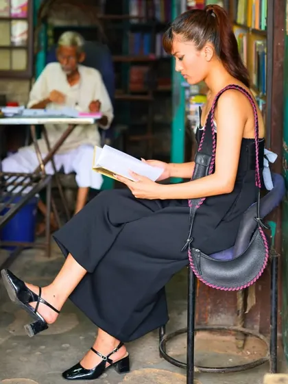 The Selena Whipstitch in black with purple stitching, seen in a quiet moment at a bookstore. It’s a bag that combines modern design with traditional craftsmanship.