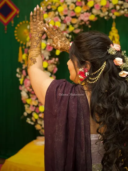 The bride showing off her intricate Mehendi design. Her hairstyle, with its delicate floral chain, perfectly complements the festive and celebratory atmosphere.