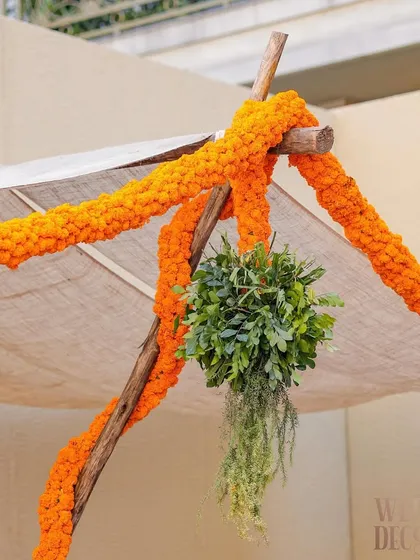 A detail shot of the tent canopy, where rustic wooden poles are wrapped in thick marigold garlands and accented with hanging green foliage.