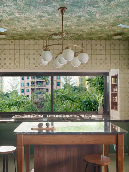 This kitchen, with its view of the lush outdoors, is the heart of the home, designed for slow mornings and shared meals. The island becomes a natural gathering spot, while the large window invites nature in, creating a space that feels both expansive and intimate.