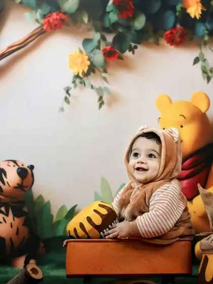 This little one, dressed in a bear costume, holds a honey pot and smiles, sitting with Winnie the Pooh and friends.