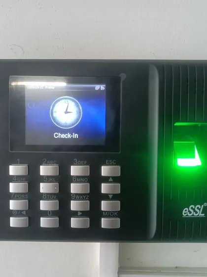 A close-up of an eSSL biometric fingerprint scanner and time attendance terminal. The green light indicates the device is active, ready to verify fingerprints for secure access or log employee check-in times.