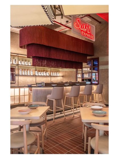 The 'Sushi Express' neon sign clearly defines the sushi bar area, using lighting as a functional and thematic tool. This is paired with a dramatic, tiered tassel chandelier to make the bar a distinct destination within the restaurant.
