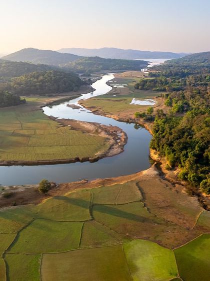 An aerial view of a river snaking through the green fields and forests of the Western Ghats in Hosanagara, Karnataka.
